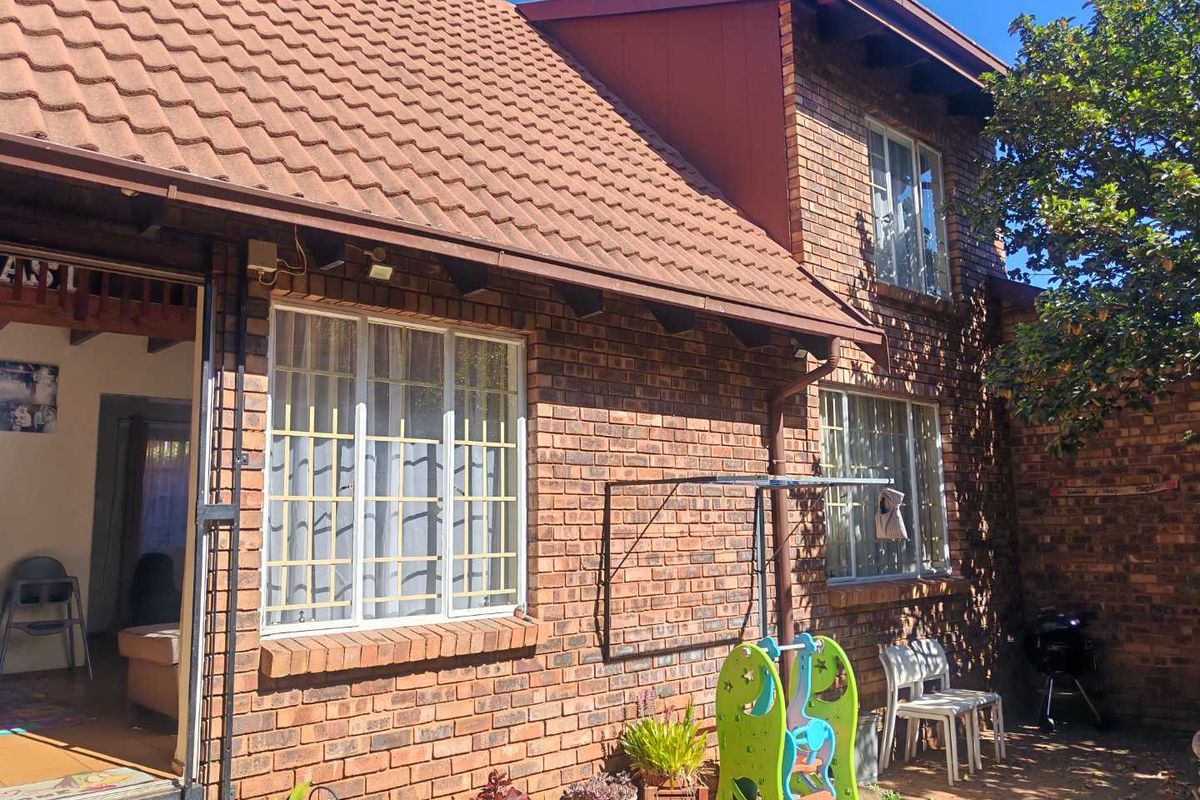 Rear view of a face brick townhouse featuring a tiled roof, security bars on windows, and a paved outdoor area.