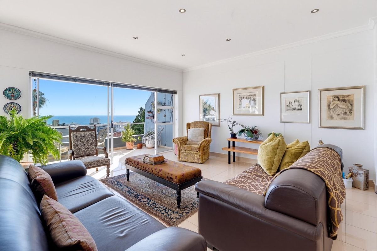 A bright and spacious living room featuring large sliding glass doors that open onto a balcony with expansive ocean views.