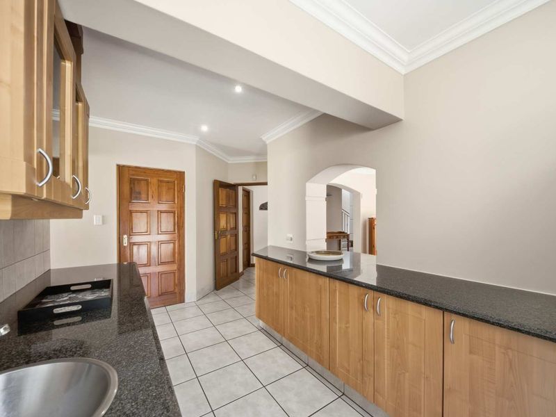 A functional kitchen featuring granite countertops, light wood cabinetry, and tiled flooring, leading into an adjacent hallway with solid wood doors.