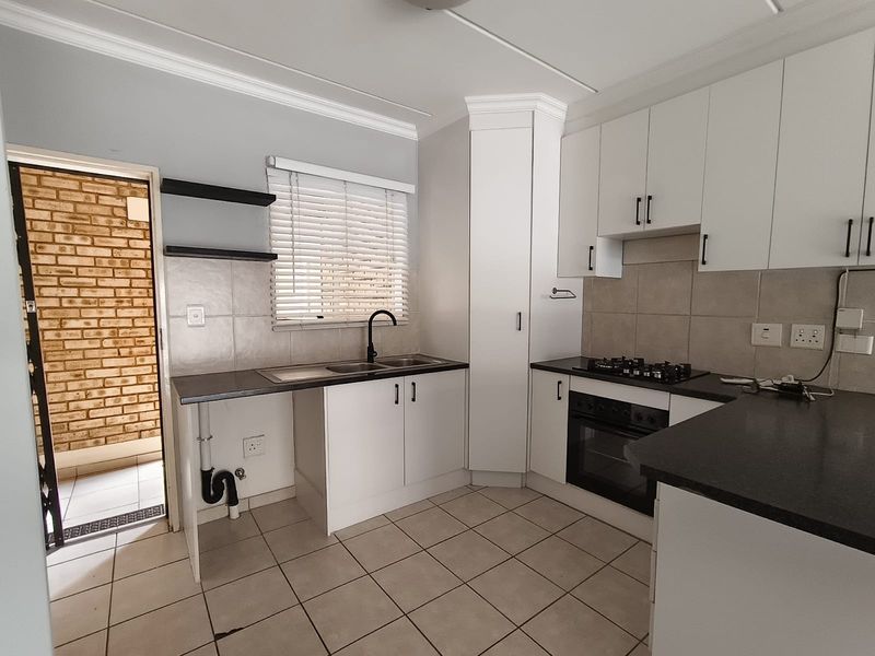 Modern kitchen featuring white cabinetry, dark countertops, built-in oven, gas hob, and tiled flooring with direct access to an exterior area.