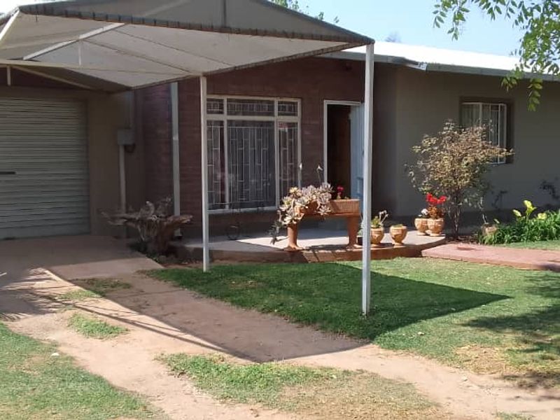 Front exterior view of a single-story house featuring a covered carport, brick facade accents, and a well-maintained front garden.