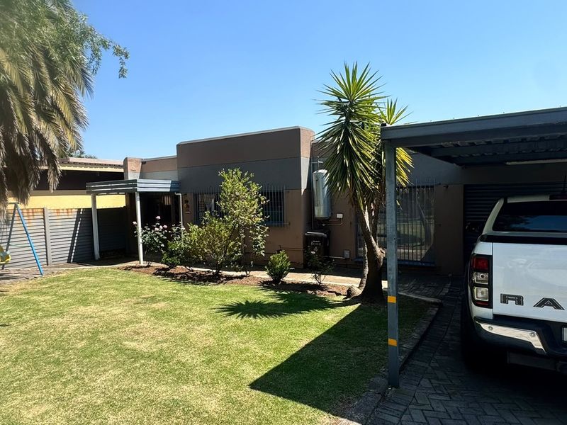 Front exterior view of the cluster property featuring a paved driveway, carport, and a well-maintained garden area.