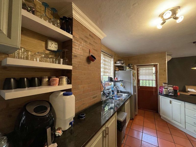 A functional kitchen featuring granite countertops, exposed brick accents, timber wall cladding, and terracotta floor tiles with direct access to the exterior.