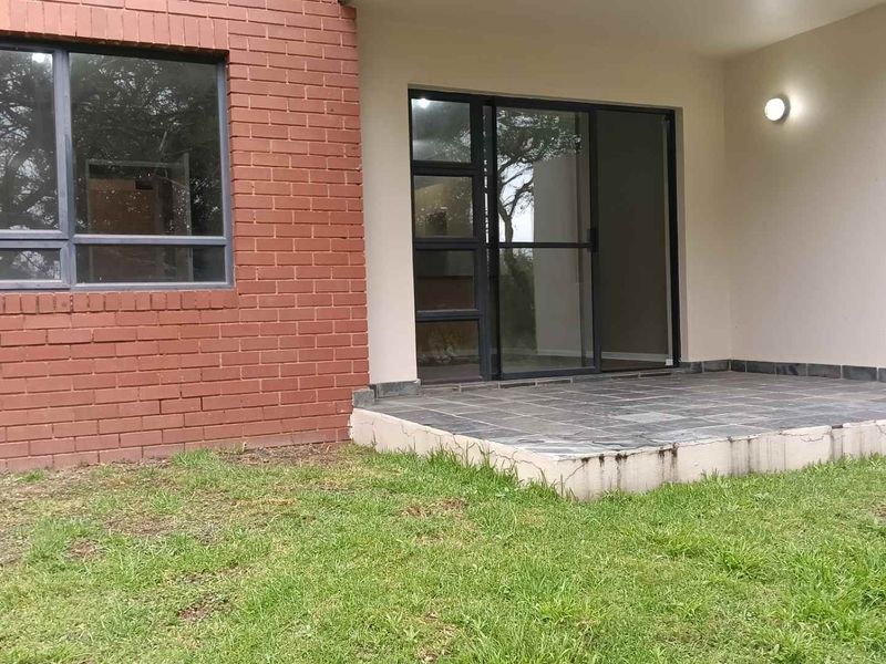 A covered patio area featuring slate tile flooring, a brick exterior wall, and sliding glass doors leading into the apartment.