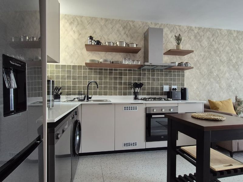 Modern open-plan kitchen featuring sleek cabinetry, stone countertops, integrated appliances, and stylish tiled backsplash, seamlessly flowing into the living area.