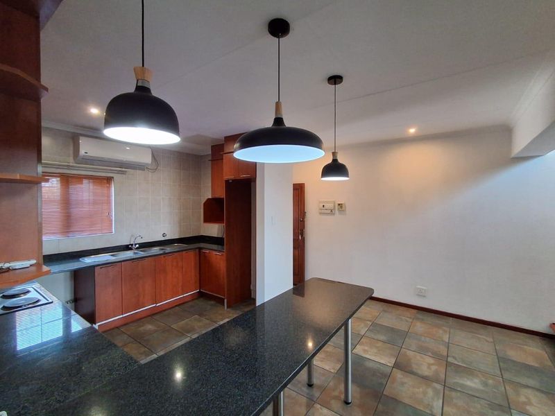 Open-plan kitchen featuring granite countertops, wooden cabinetry, a built-in hob, and tiled flooring, complemented by modern pendant lighting and an air conditioning unit.