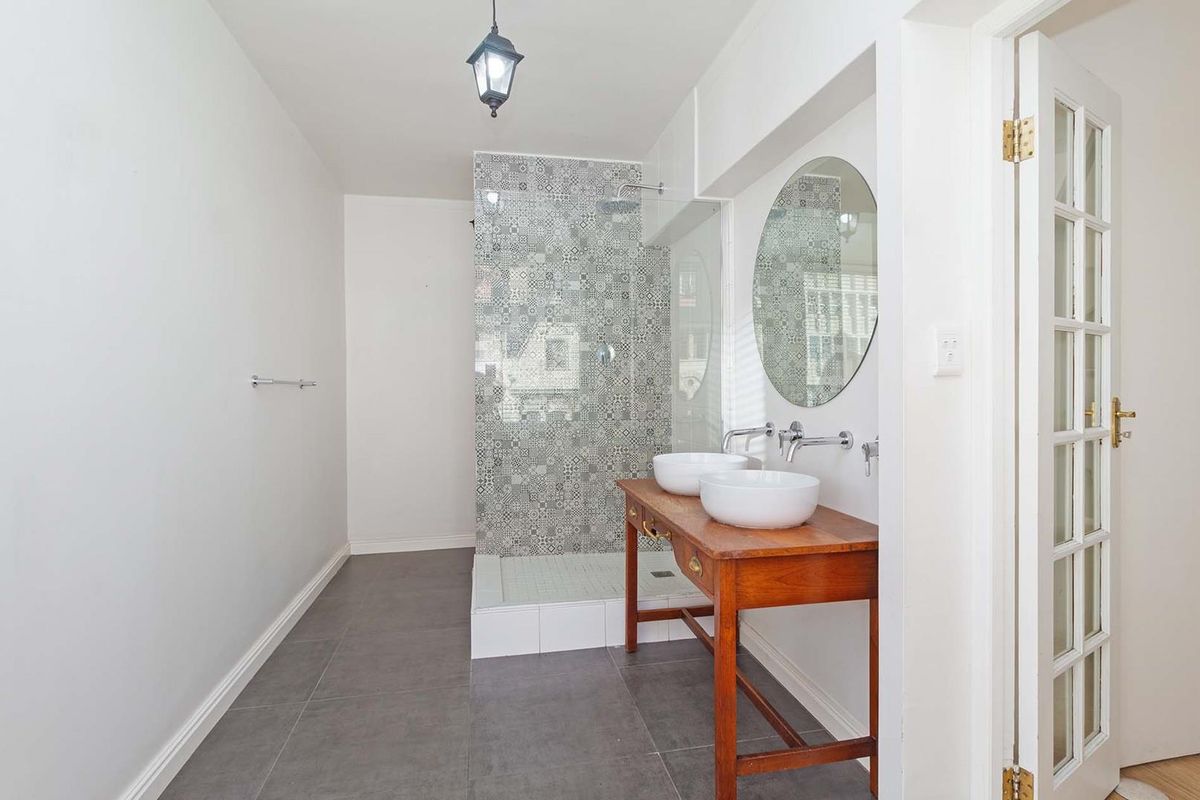 A modern bathroom featuring a walk-in shower with patterned tile accents, a double vanity with vessel sinks, and grey floor tiling.