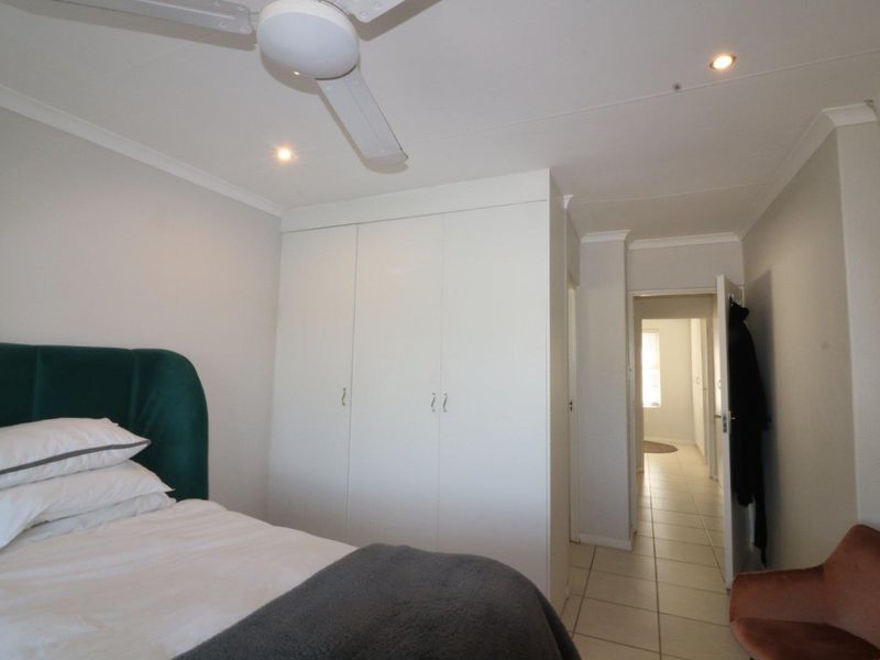A bedroom featuring built-in cupboards, tiled flooring, and a ceiling fan, with a view leading into the hallway.