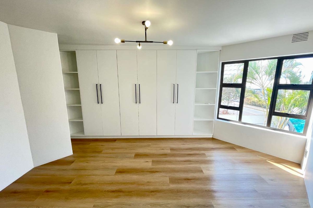 A bright, modern bedroom featuring extensive built-in floor-to-ceiling cabinetry with integrated shelving and durable wood-look flooring.