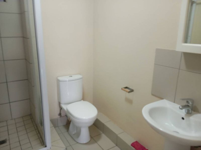 A functional bathroom featuring a shower enclosure, pedestal basin, and toilet with neutral tiled flooring and wall finishes.