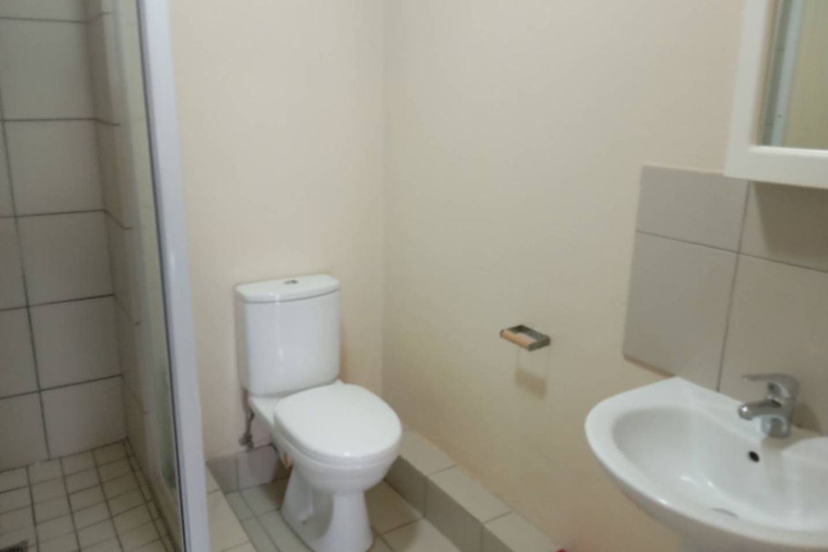 A functional bathroom featuring a shower enclosure, pedestal basin, and toilet with neutral tiled flooring and wall finishes.