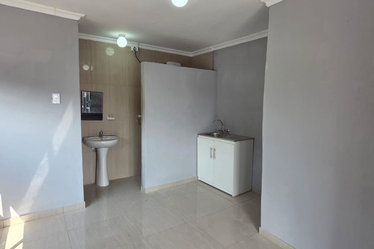 An open-plan studio space featuring tiled flooring, a pedestal basin, and a basic kitchen sink cabinet unit.