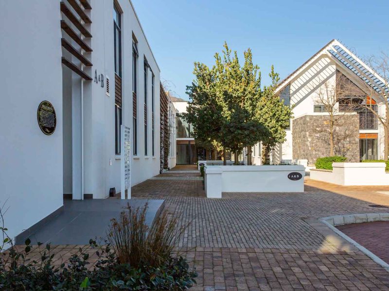 A well-maintained commercial courtyard featuring paved walkways, stone masonry accents, and modern architectural timber detailing between two professional building structures.