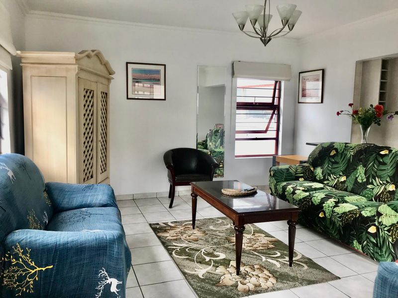 A bright living room featuring tiled flooring, a large louvre window, and decorative ceiling coving, providing a functional and well-lit space.