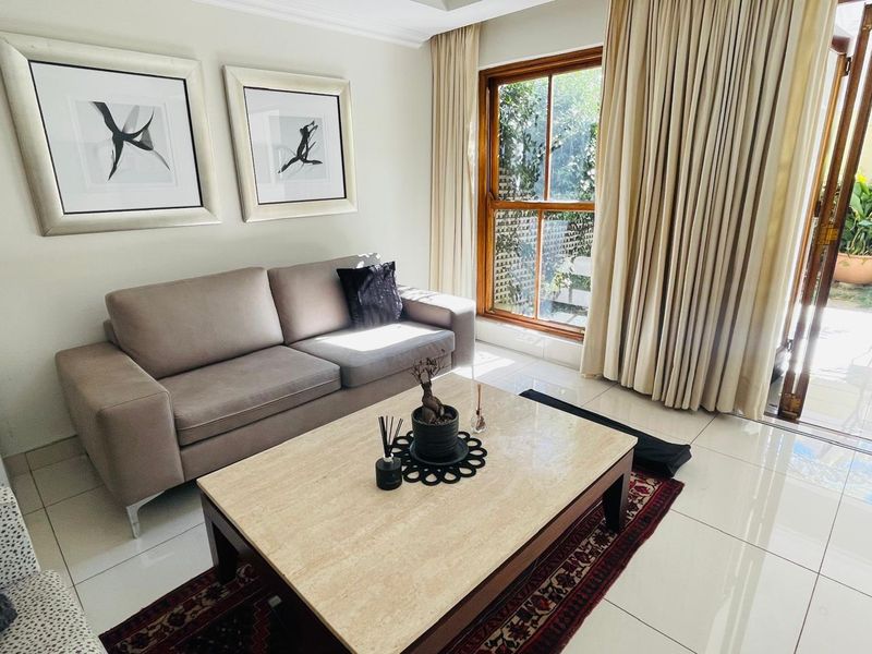 A bright and well-maintained living room featuring large format floor tiles, timber-framed windows, and direct access to an outdoor area.