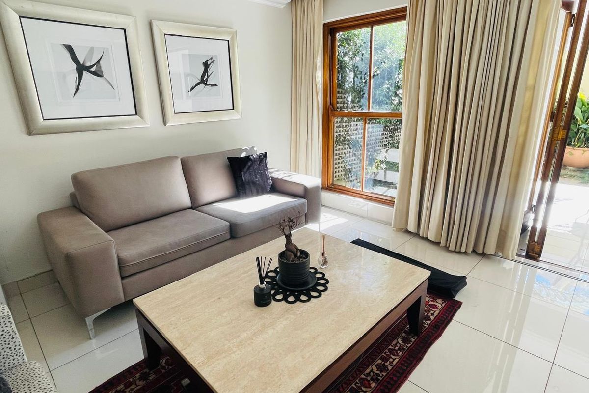 A bright and well-maintained living room featuring large format floor tiles, timber-framed windows, and direct access to an outdoor area.