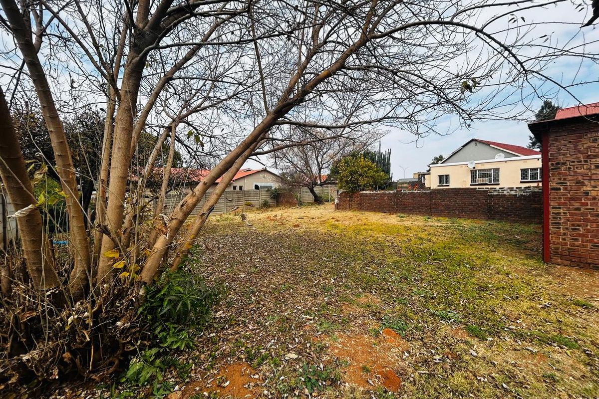 A spacious rear garden area featuring a brick boundary wall and mature trees, offering potential for landscaping and outdoor development.