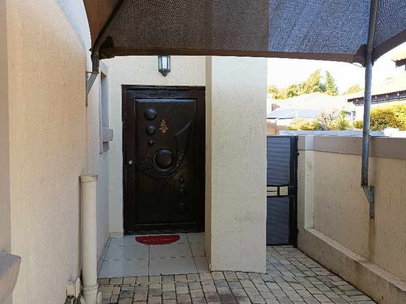 A private entrance area featuring a paved courtyard, a shade sail for cover, and a secure front door.