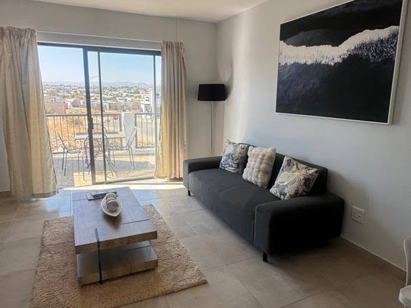 Bright living room featuring large sliding glass doors that open onto a balcony with scenic views and neutral tiled flooring throughout.