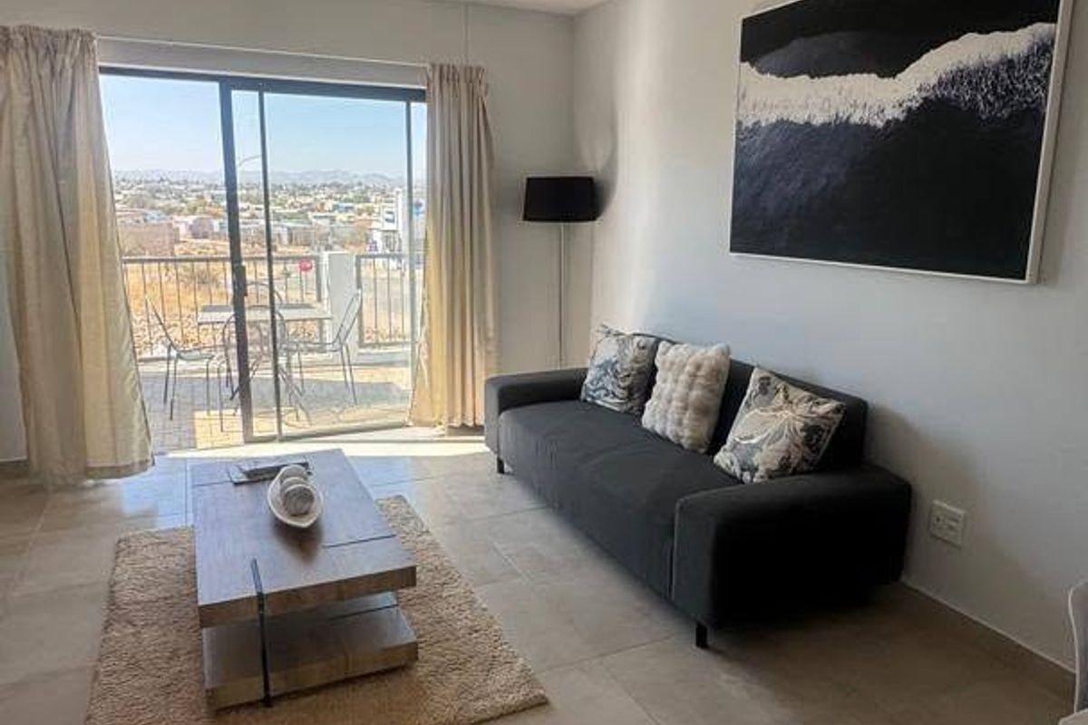 Bright living room featuring large sliding glass doors that open onto a balcony with scenic views and neutral tiled flooring throughout.