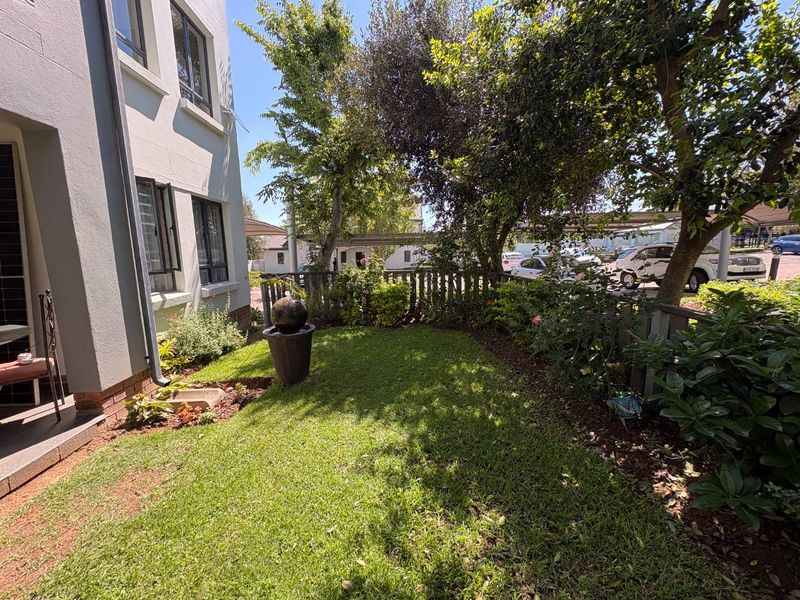 A well-maintained private garden area featuring a lush lawn, established trees, and perimeter fencing, adjacent to the apartment building's exterior.
