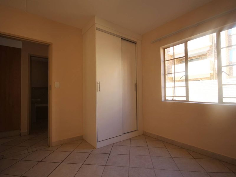 A bright, empty bedroom featuring tiled flooring, a built-in sliding door wardrobe, and a window with security bars.