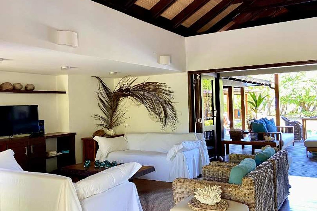 Spacious living room featuring high exposed timber beam ceilings, polished timber flooring, and seamless indoor-outdoor flow through bi-fold doors to the patio.