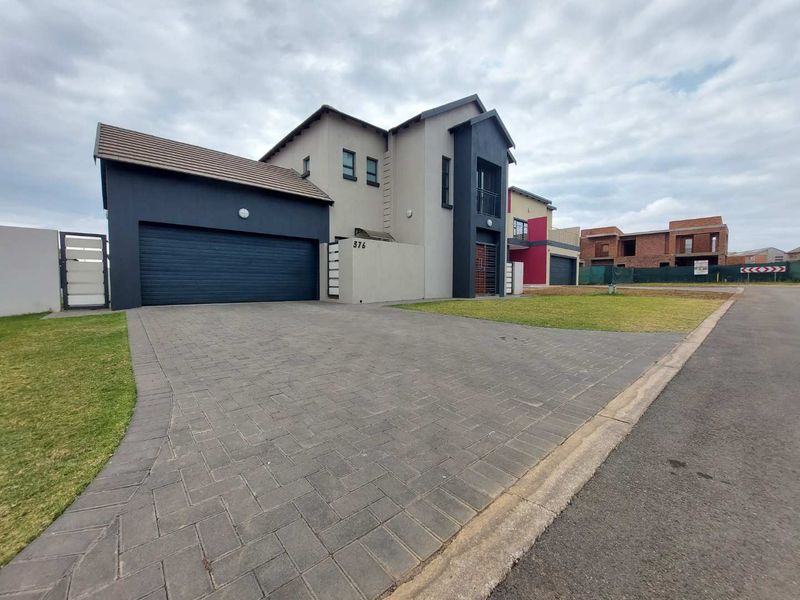 Modern double-story residential home featuring a paved driveway, double garage, and a balcony, situated in a contemporary estate setting.