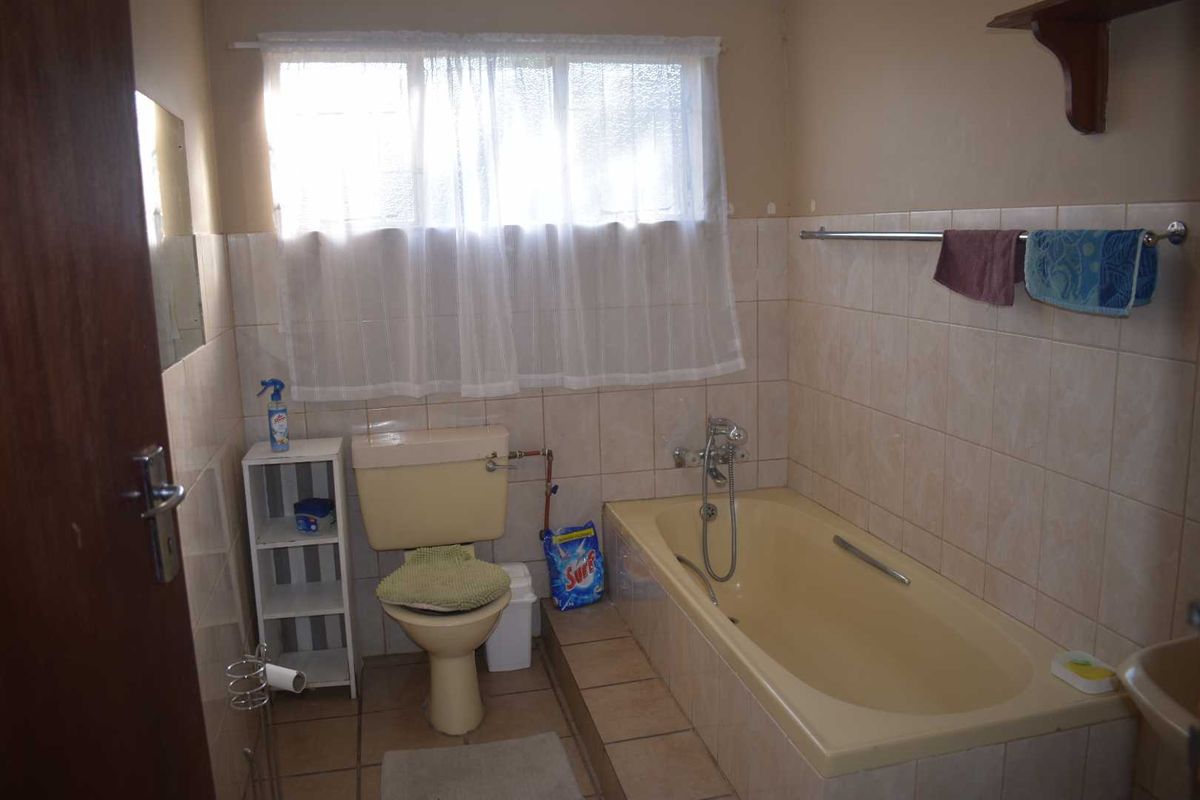 A dated bathroom featuring a built-in bathtub, toilet, and tiled finishes, offering potential for a modern renovation.
