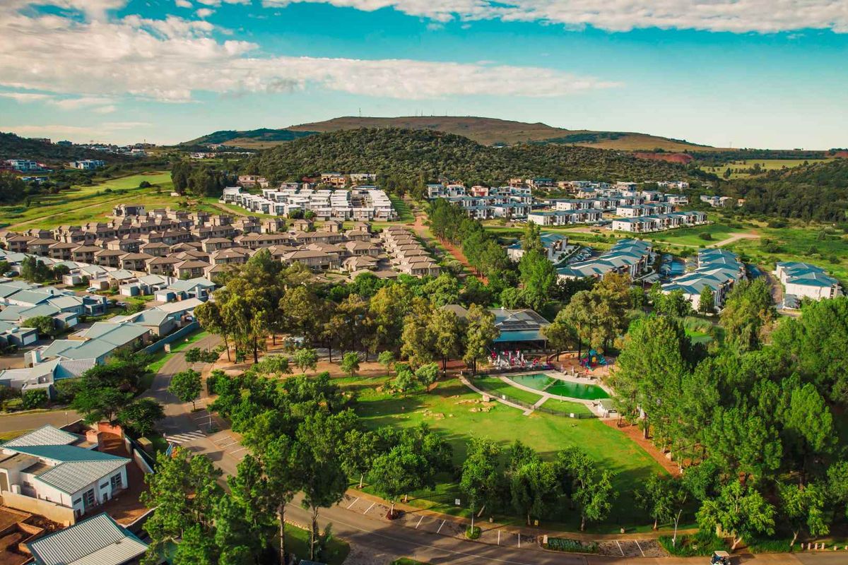 Aerial view of a residential apartment estate featuring landscaped green spaces, communal swimming pool, and surrounding suburban infrastructure.