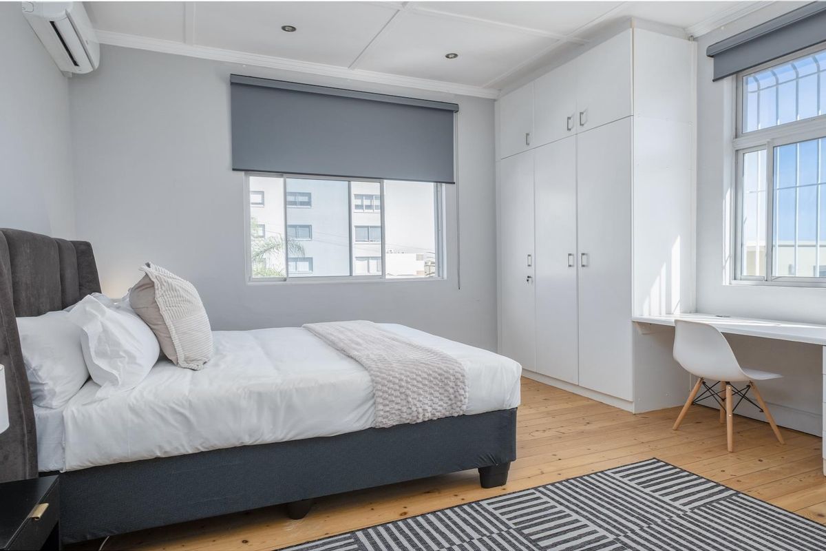A well-maintained bedroom featuring timber flooring, built-in cupboards, an integrated desk, and a split-system air conditioner.
