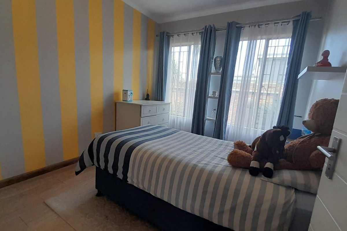 A bedroom featuring striped accent wall, tiled flooring, and large windows with security bars, providing natural light.