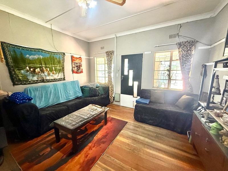 A living room featuring hardwood flooring, security bars on windows, and a modern front door, requiring cosmetic updates to the walls and ceiling.