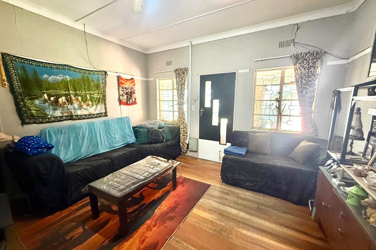 A living room featuring hardwood flooring, security bars on windows, and a modern front door, requiring cosmetic updates to the walls and ceiling.