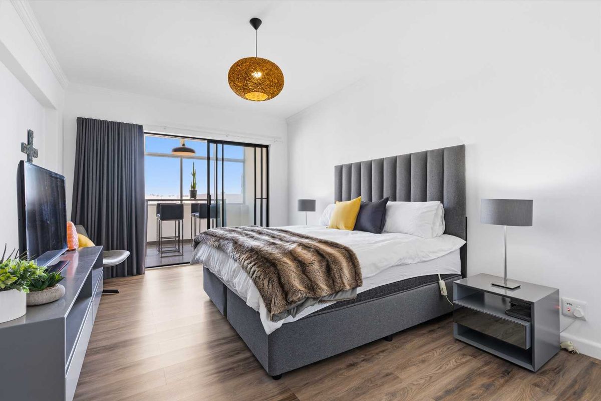 A well-maintained bedroom featuring laminate flooring and a sliding glass door providing direct access to a private balcony.