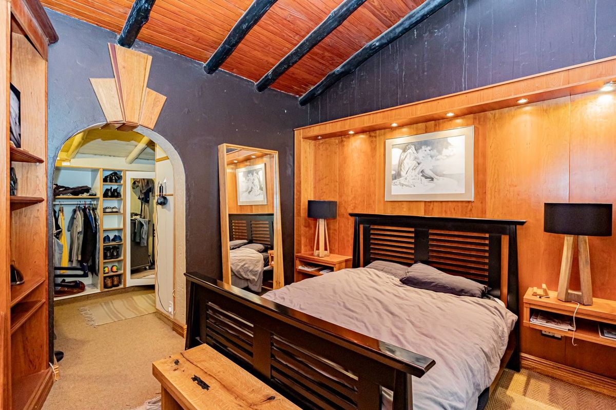 Bedroom featuring a timber ceiling with exposed beams, built-in timber headboard with integrated lighting, and an adjoining walk-in closet area.