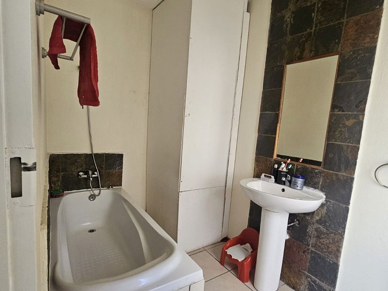 A functional bathroom featuring a bathtub, pedestal basin, and built-in storage cupboard with dark tiled splashbacks.