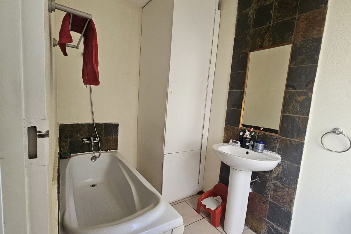 A functional bathroom featuring a bathtub, pedestal basin, and built-in storage cupboard with dark tiled splashbacks.