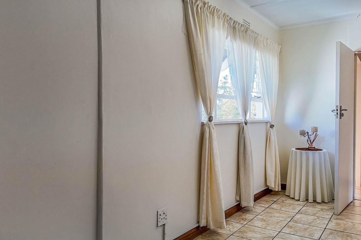 A bright interior space featuring tiled flooring, a window with curtain fixtures, and a doorway leading to an adjacent room.