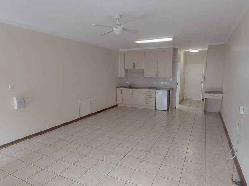 Spacious open-plan living area featuring tiled flooring, a ceiling fan, and a functional kitchenette with built-in cabinetry and a sink.