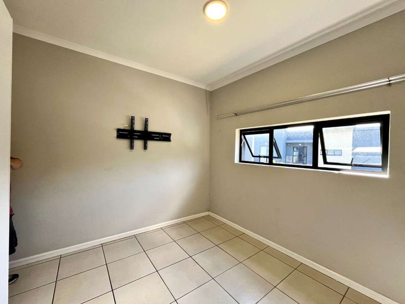 An empty bedroom featuring neutral wall paint, tiled flooring, and a wall-mounted TV bracket, offering a clean and versatile space.