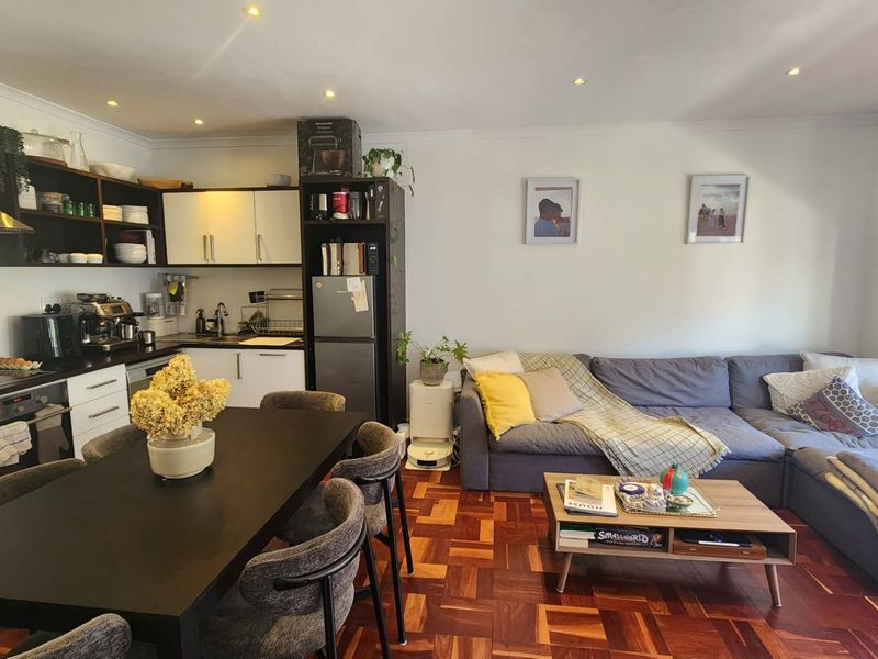 An open-plan living and kitchen area featuring classic parquet flooring, modern cabinetry, and integrated kitchen appliances, creating a functional and cohesive living space.