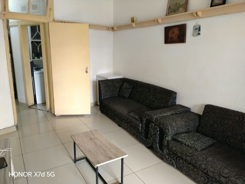 A living room area featuring tiled flooring and built-in wooden wall shelving, providing a functional space with potential for modernization.