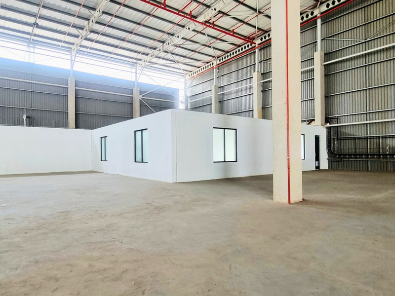 Spacious industrial warehouse interior featuring high ceilings with exposed steel trusses, concrete flooring, and a central partitioned office structure.