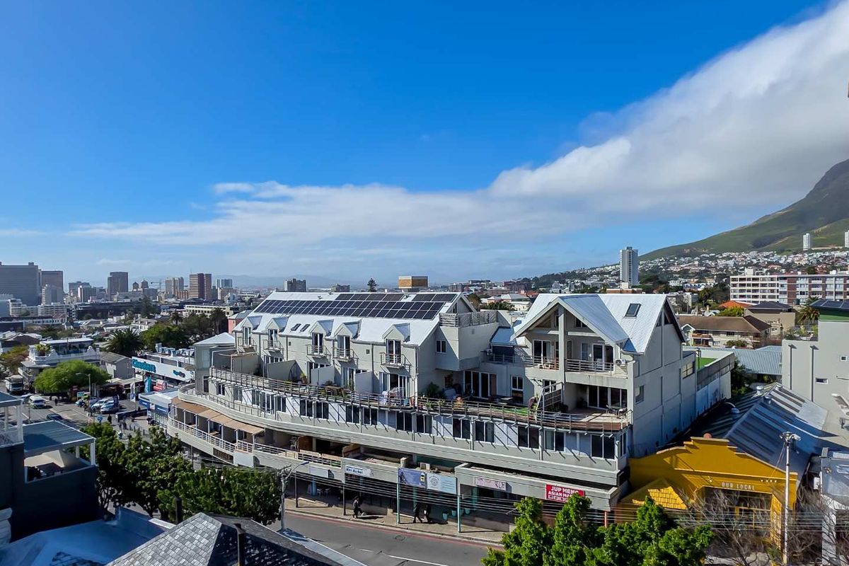 An elevated aerial view of a multi-story apartment building featuring rooftop solar panels, private balconies, and a clear view of the surrounding urban landscape.