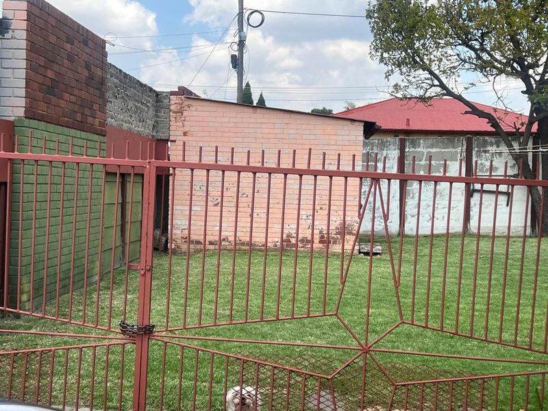 A rear garden area featuring a lawn, enclosed by a metal security gate and brick boundary walls with visible weathering.
