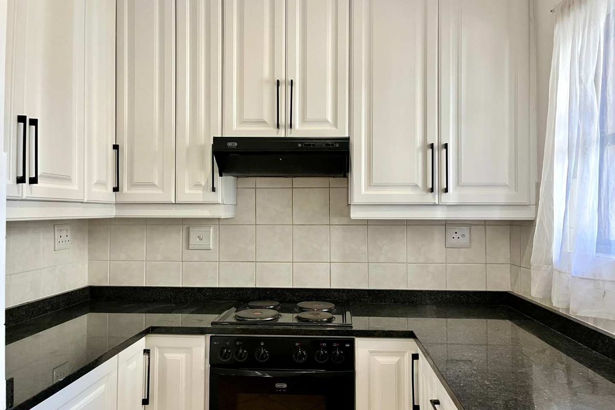 A well-maintained kitchen featuring white cabinetry, black granite countertops, a built-in oven, and an electric hob with a tiled backsplash.