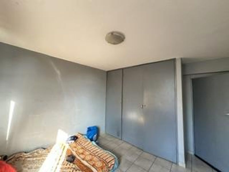 A bedroom featuring tiled flooring and built-in cupboards, requiring cosmetic updates to the wall finishes.