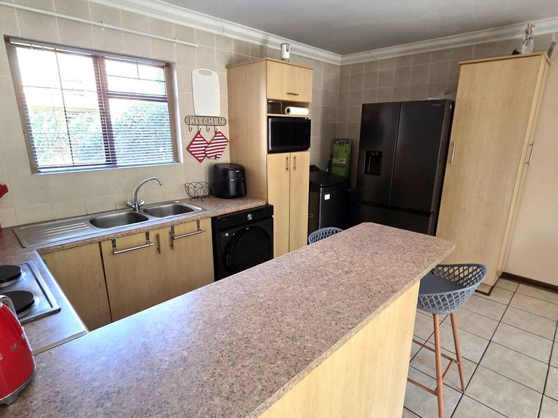 Functional kitchen featuring light wood cabinetry, laminate countertops, a breakfast bar, tiled backsplash, and integrated appliances, offering a practical layout for daily use.