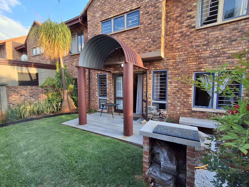 Rear exterior view of a face brick townhouse featuring a tiled patio with a unique arched metal cover and a built-in brick braai area.